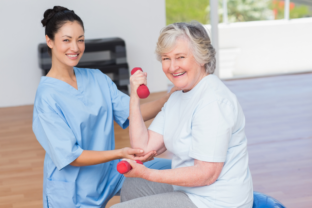 Portrait of female instructor assisting senior woman in lifting dumbbells at gym